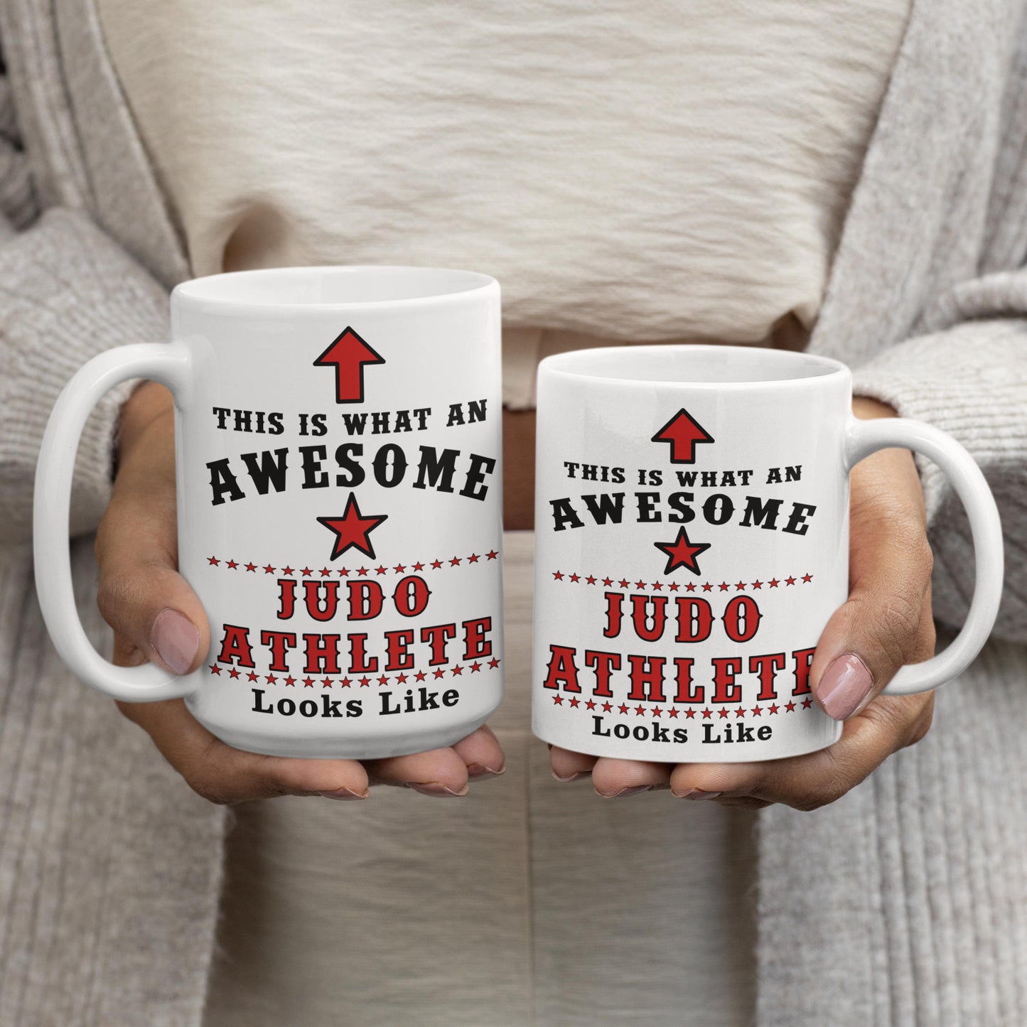 Two hands holding a 15oz and 11oz judo athlete mug side by side, both printed with "This is what an awesome Judo Athlete looks like" design, showing size comparison