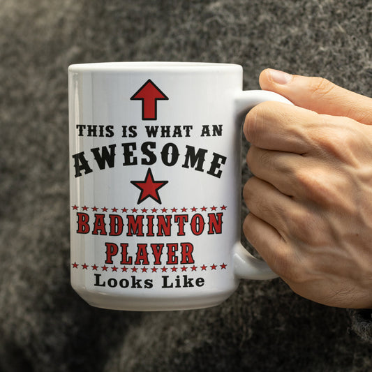 Hand holding a white 15oz badminton player mug showing the red and black "Awesome Badminton Player" print up close