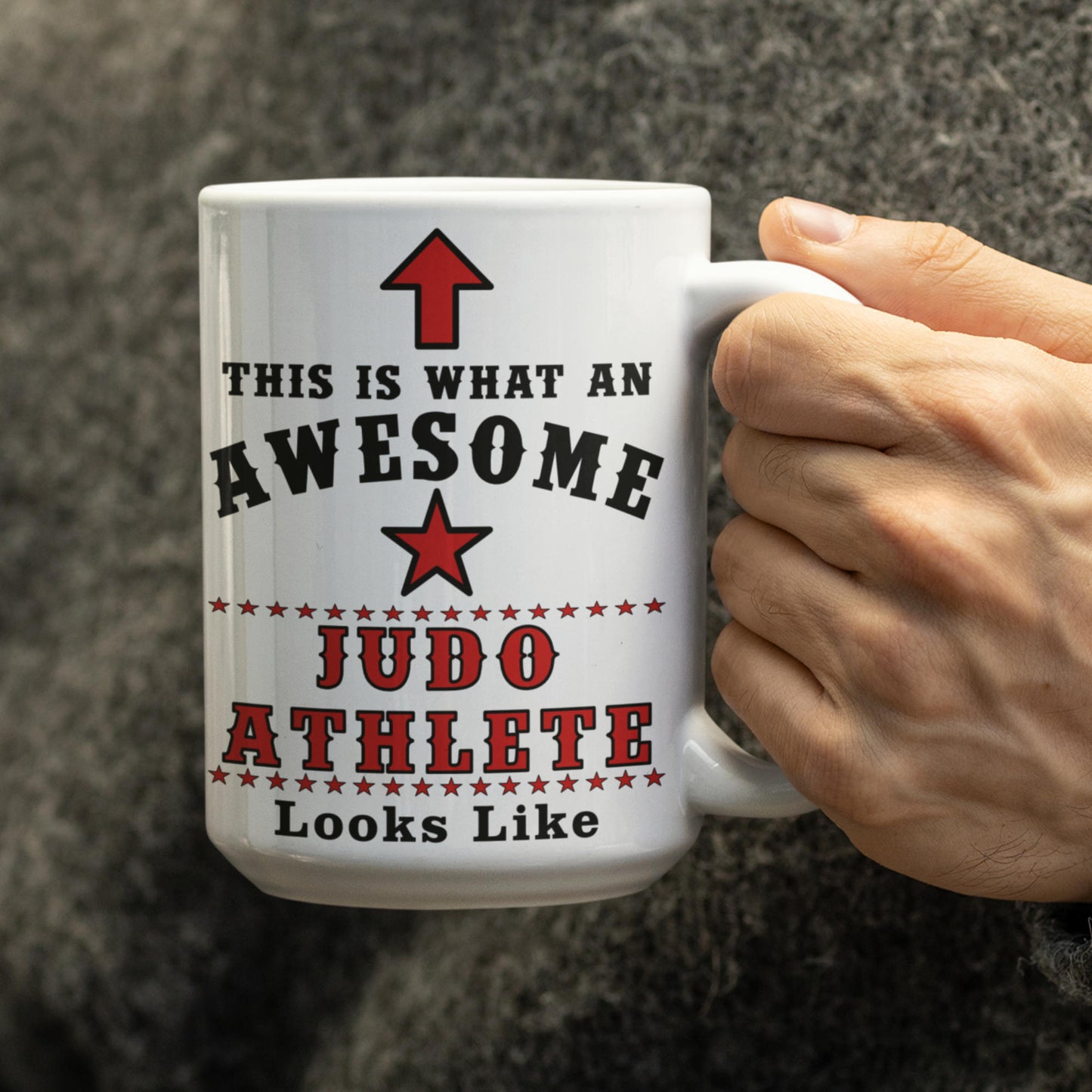 Person holding white 15oz mug printed with "This is what an awesome Judo Athlete looks like" in black and red text with star and arrow design