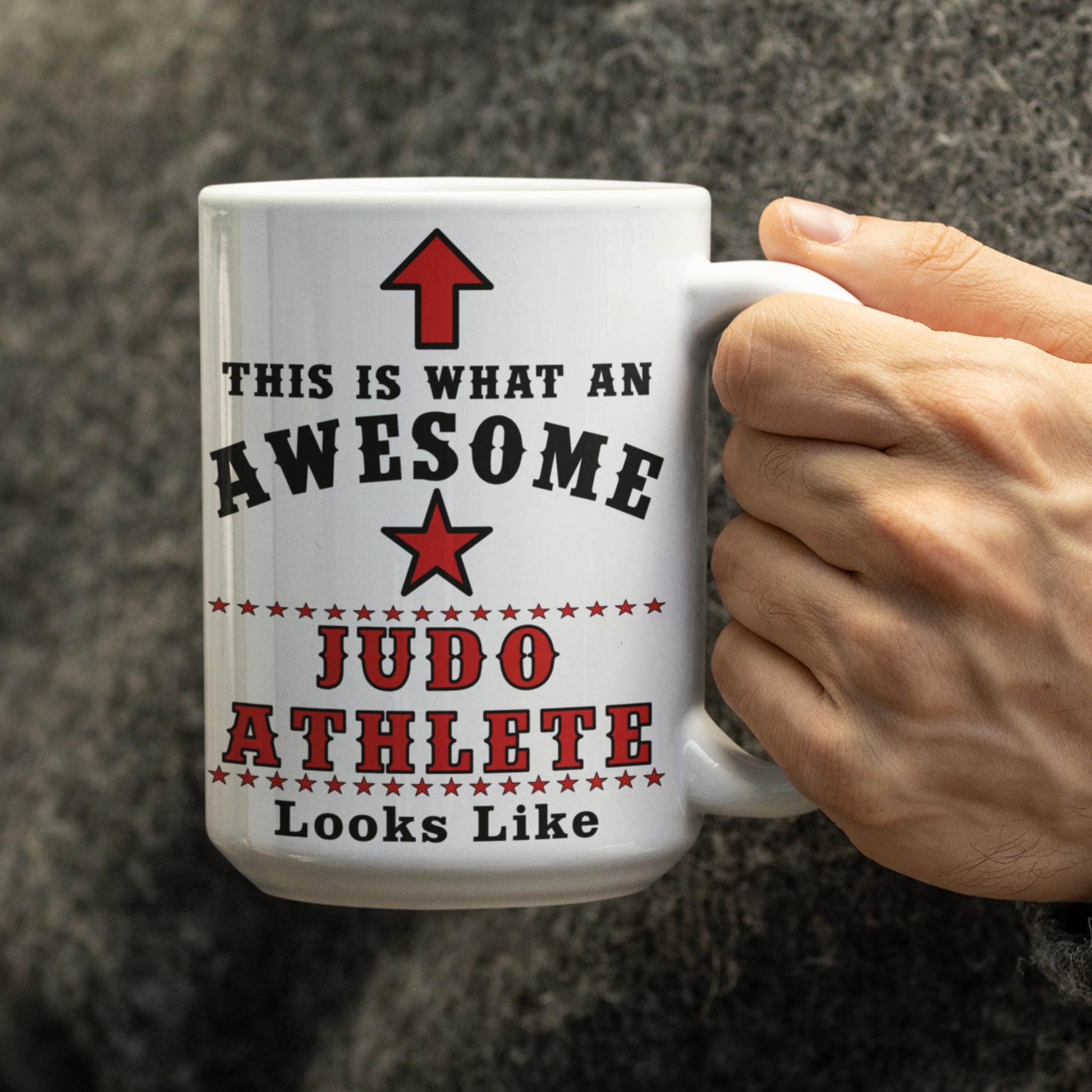 Person holding white 15oz mug printed with "This is what an awesome Judo Athlete looks like" in black and red text with star and arrow design