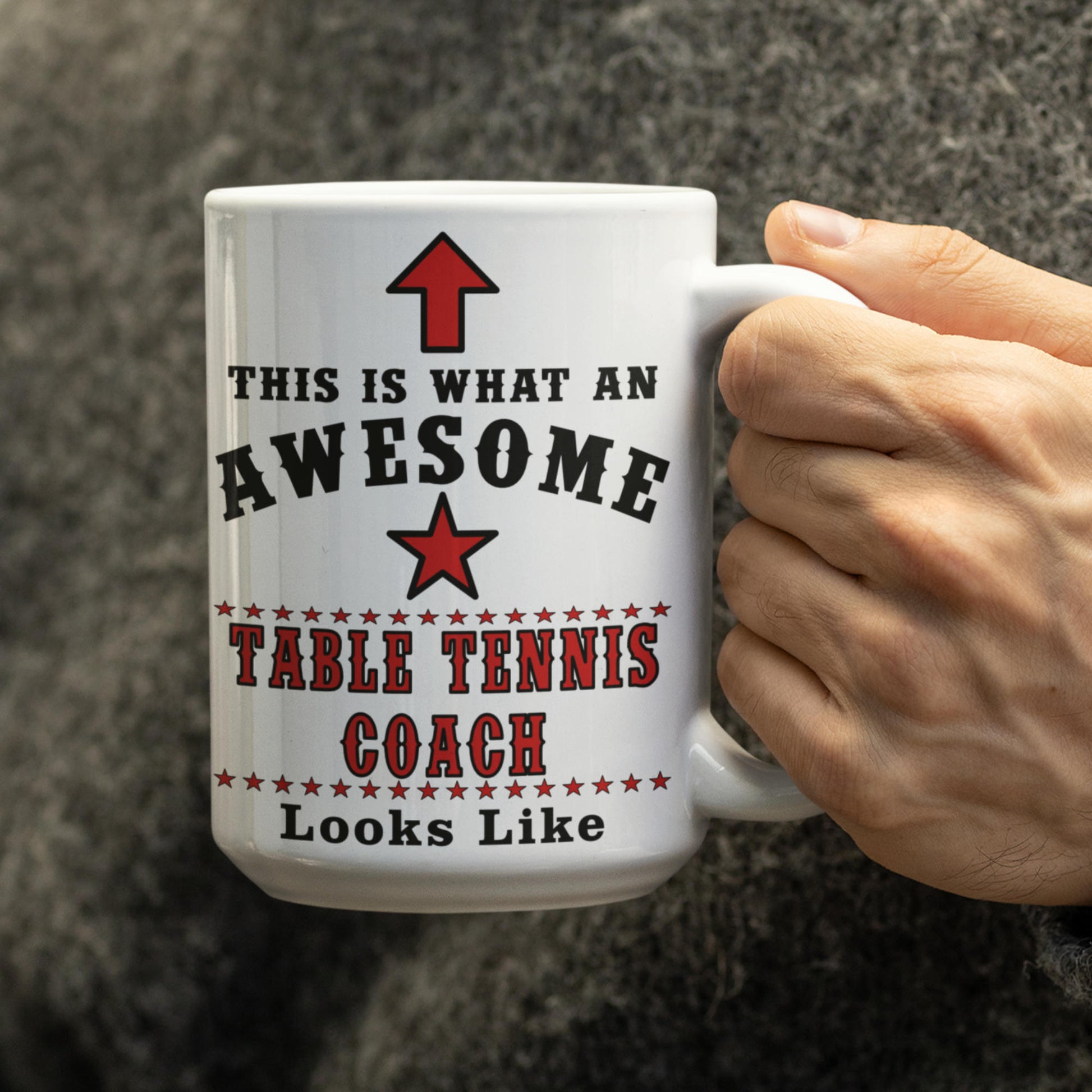 Close-up of hand holding white 15oz Awesome Table Tennis Coach mug with red star design