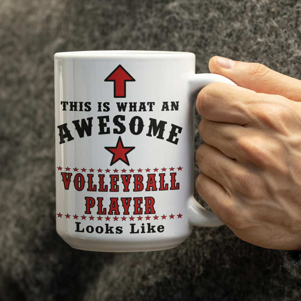 Close-up of a hand holding the 15oz "Awesome Volleyball Player" mug against a grey background, showing red star and arrow design detail