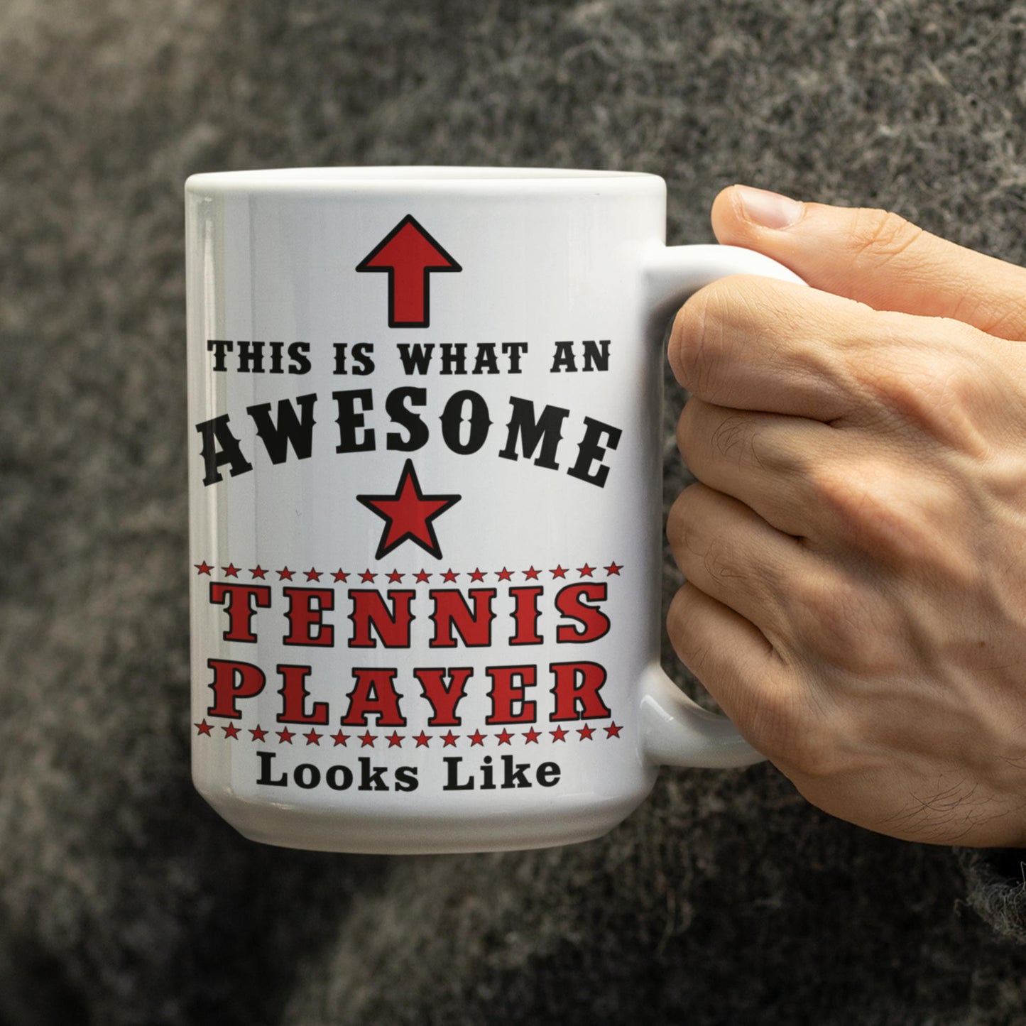 Close-up of hand holding a 15oz white mug printed with "This Is What An Awesome Tennis Player Looks Like" in bold red and black lettering