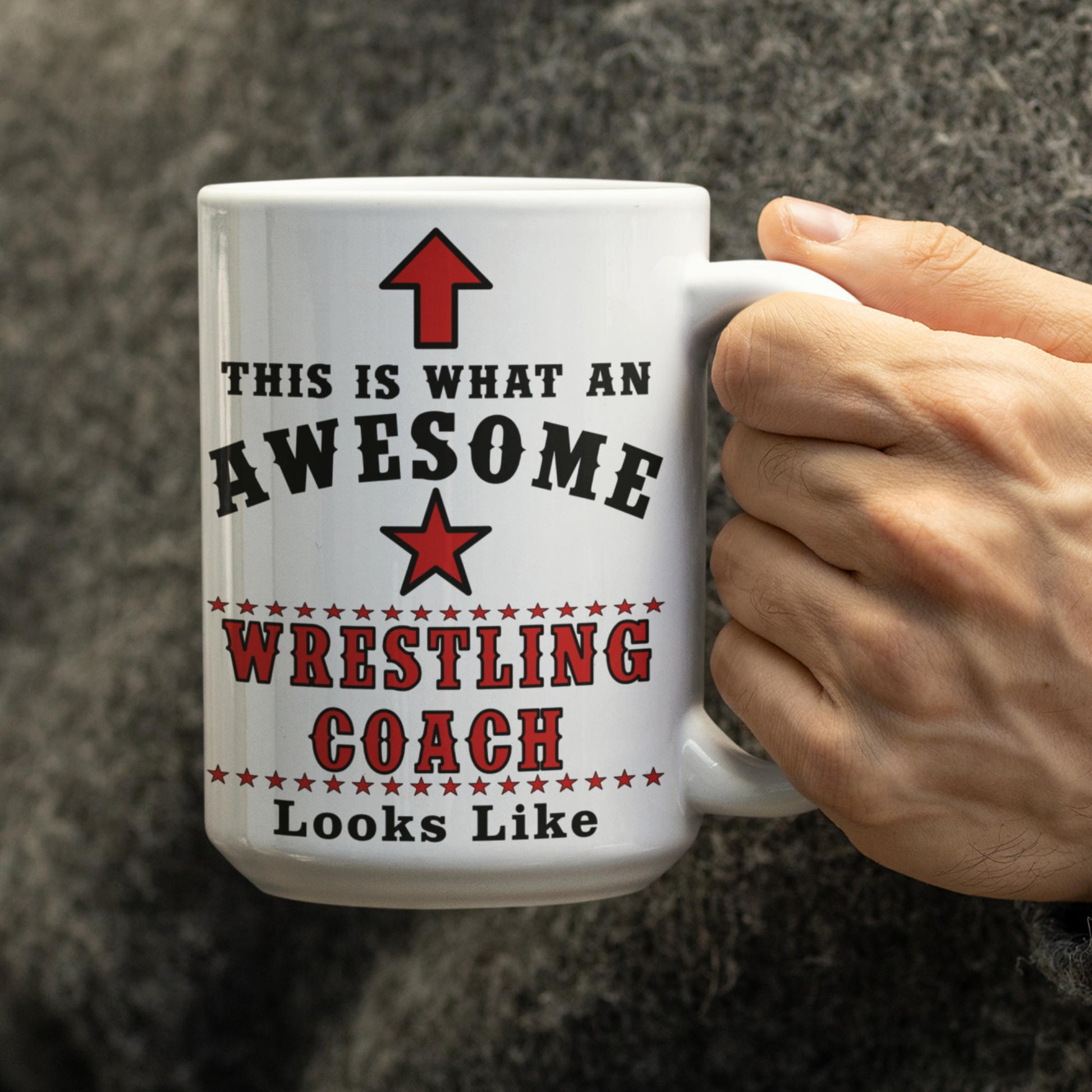 Person holding a large 15oz "Awesome Wrestling Coach" white ceramic mug in hand against a neutral grey sweater background.