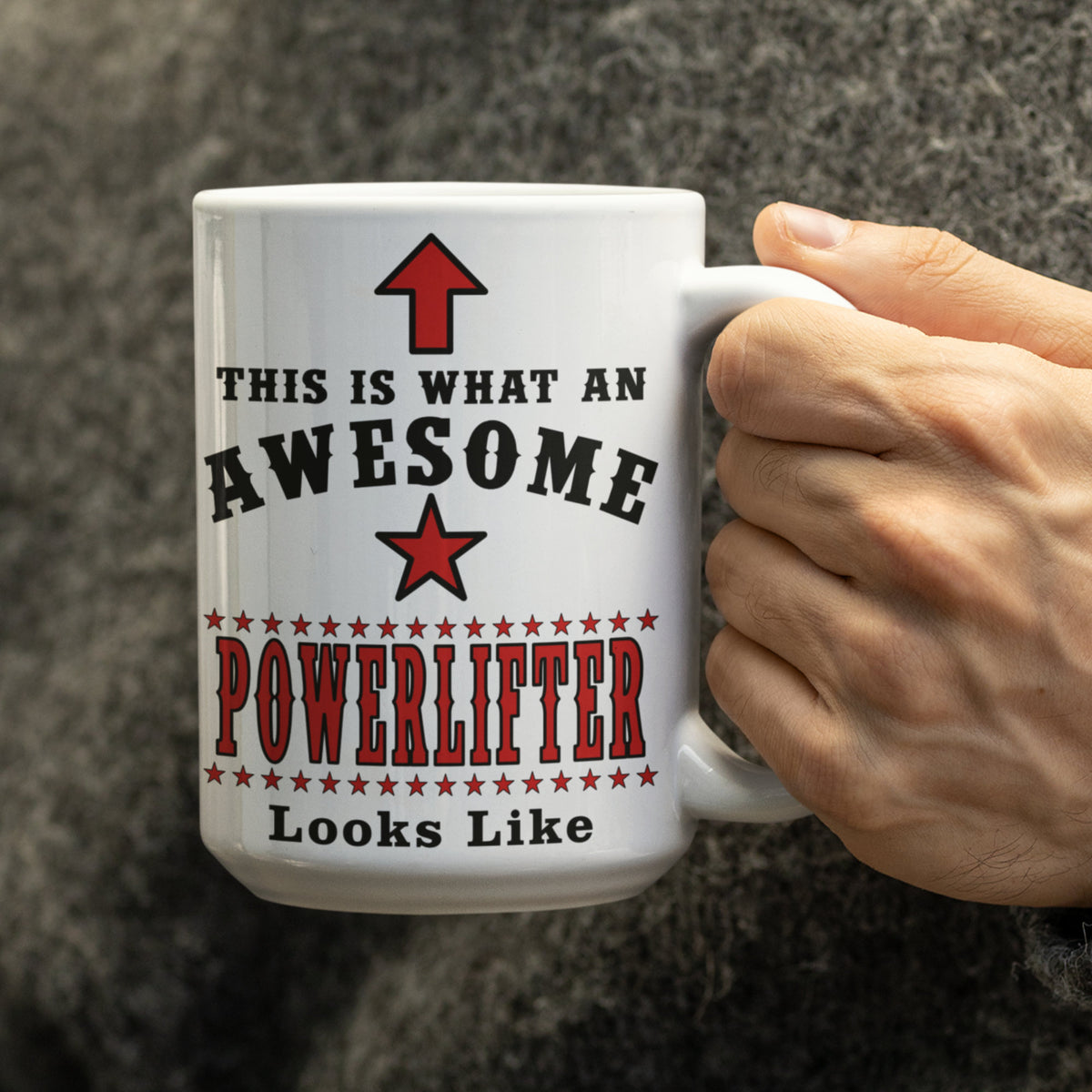 Hand holding a white 15oz "Awesome Powerlifter" mug with red and black text design