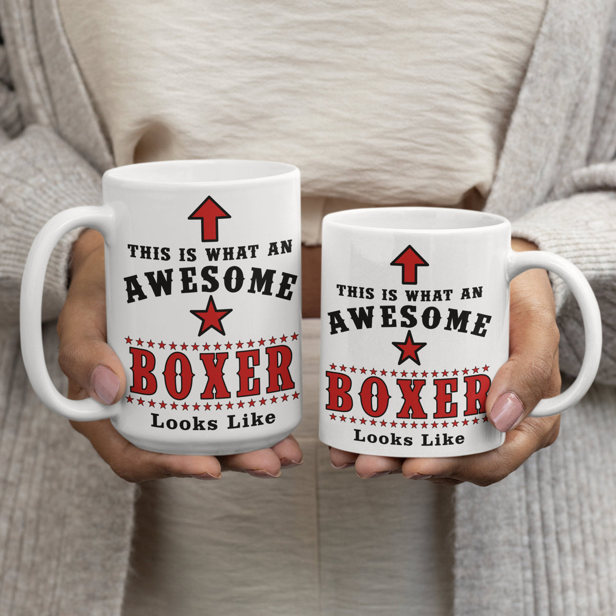 Woman holding two white ceramic mugs printed with "This Is What An Awesome Boxer Looks Like" in red and black boxing-style lettering, comparing 15oz and 11oz sizes