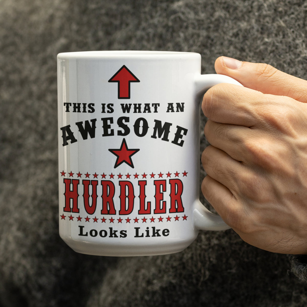 Close-up of a hand holding the white 15oz Hurdler mug with red and black "This is what an awesome Hurdler Looks Like" design