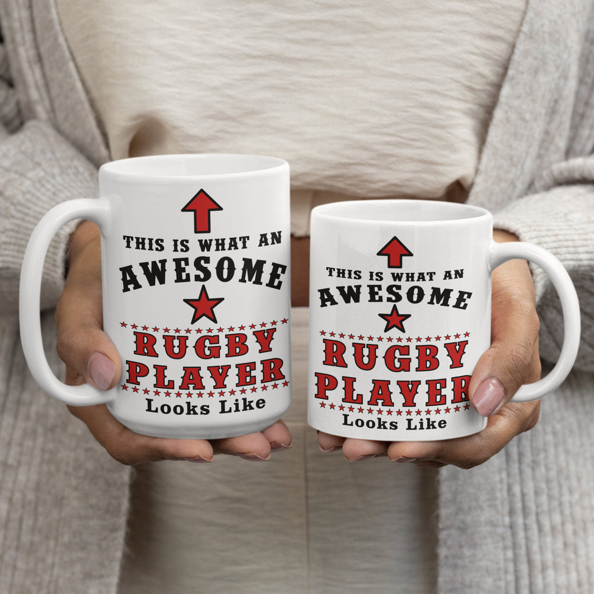 Two hands holding 15oz and 11oz rugby player mugs side by side, both printed with "This Is What An Awesome Rugby Player Looks Like"