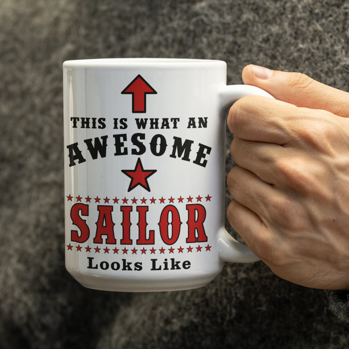 Close-up of hand holding white 15oz "This Is What An Awesome Sailor Looks Like" mug with red star and stripe design