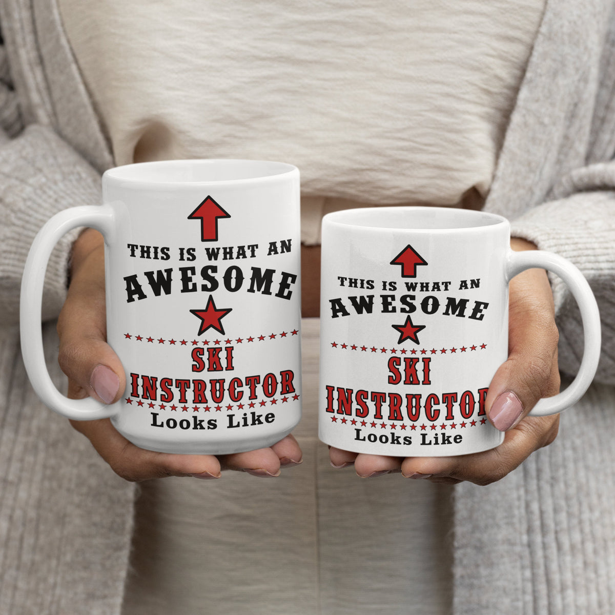 Person holding a 15oz and 11oz white ceramic mug printed with "This Is What An Awesome Ski Instructor Looks Like" in black and red text with a star and arrow design
