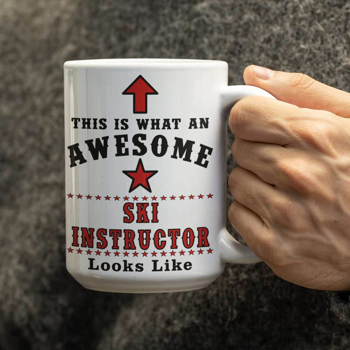 Close-up of a hand holding a 15oz white ceramic mug reading "This Is What An Awesome Ski Instructor Looks Like" with red star and arrow graphic