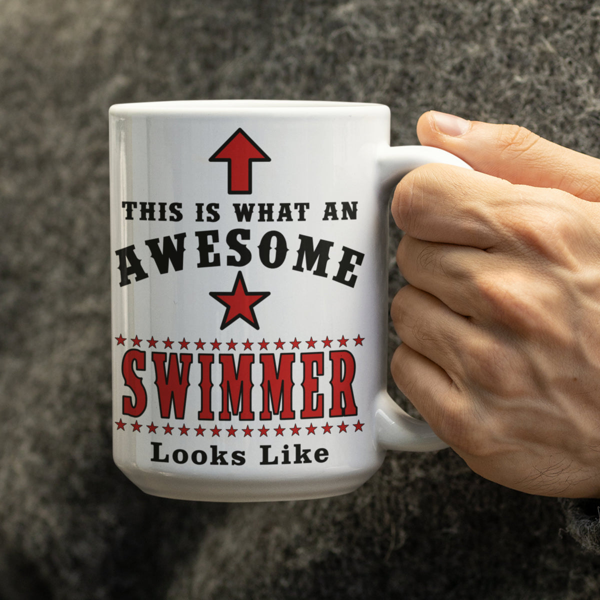 Person in a grey jumper holding a large 15oz Awesome Swimmer mug with red star and arrow design